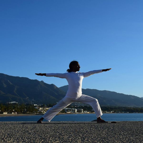 Man doing a powerful warrior yoga pose outdoors at sunrise.